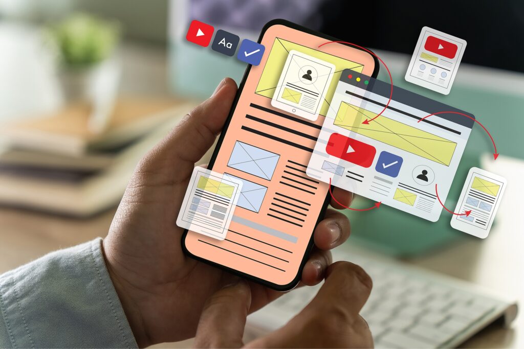 A businessman's hand working on a computer, with a UI designer brainstorming in the background, highlighting the importance of a consistent user journey and responsive design in reducing bounce rates and increasing conversion rates across various devices.